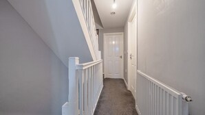 A narrow hallway with white railings, a carpeted floor, and a door at the end. - Four-bedroom home with garden, workspace and easy city access (West Midlands)
