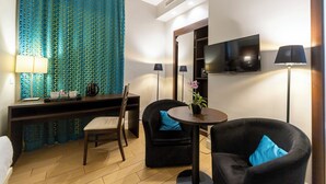 Une chambre d’hôtel compacte comprenant un bureau, deux chaises, un téléviseur et une petite table agrémentée d’une plante.