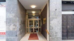 L’entrée d’un hôtel, avec une façade en marbre, un tapis rouge et une porte à deux battants dotée de panneaux de verre.