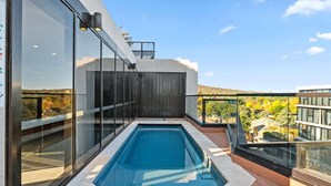 A rooftop swimming pool with glass walls and a wooden deck, overlooking a residential area. - Bright Unit with Secure Parking and Garden Access (Reid)
