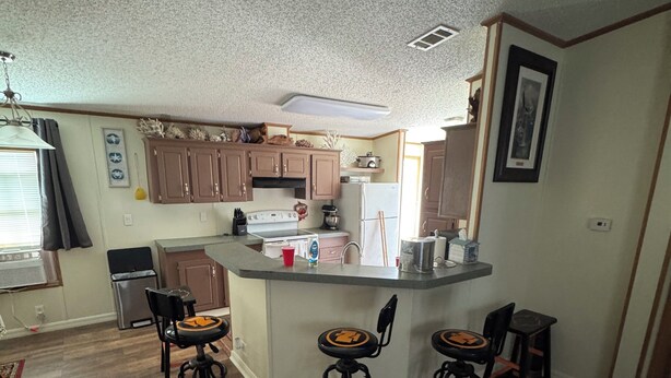 A compact kitchen with a central island, wooden cabinets, and three stools.