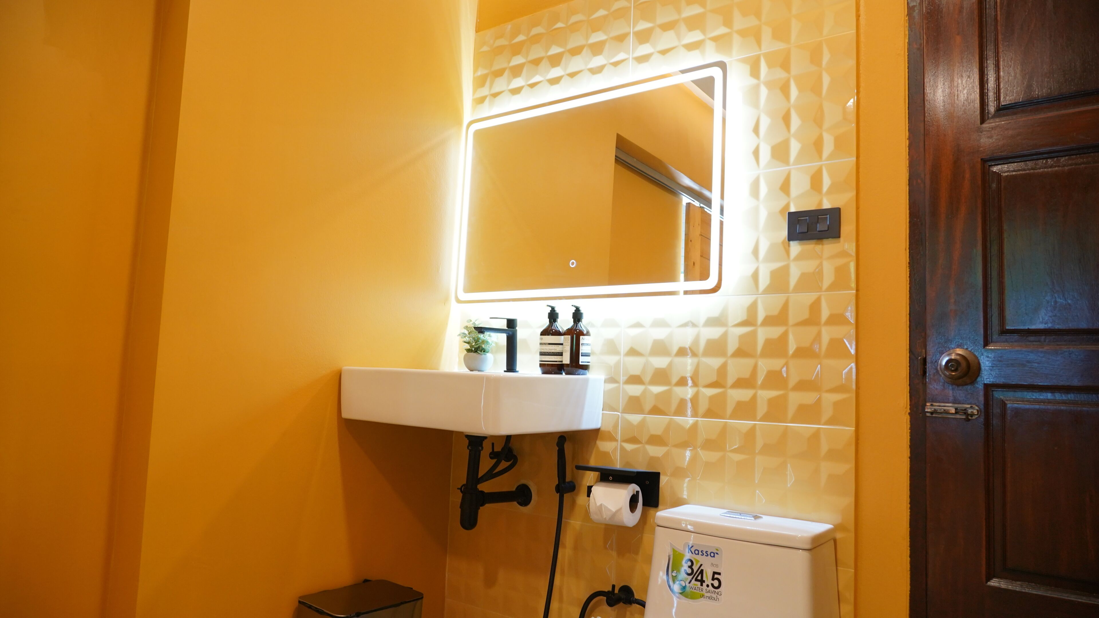 A bathroom with a white sink, a mirror, a toilet, and a small trash bin.