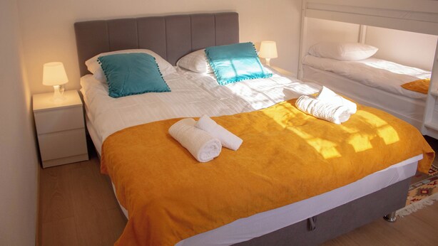 A double bed with an orange bedspread, two pillows, and two rolled towels. - Studio apartment for 4 people #1 (Sarajevo)