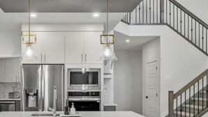 Eine moderne Küche mit Edelstahlgeräten, einer zentralen Kochinsel mit Barhocker und einer Treppe, die zu einer Erschließung führt.