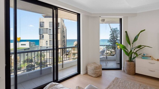 Un apartamento moderno con grandes puertas correderas de vidrio que dan a un balcón con vistas al mar y edificios.