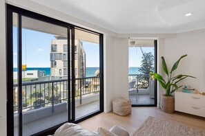 Un apartament modern amb grans portes corredisses de vidre que donen a un balcó amb vista al mar i els edificis.