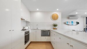 Una cocina moderna con armarios blancos, suelo de madera, un reloj en la pared y una decoración con una tabla de surf.