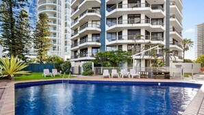 Una piscina con sillones de descanso y un edificio de varios pisos al fondo.