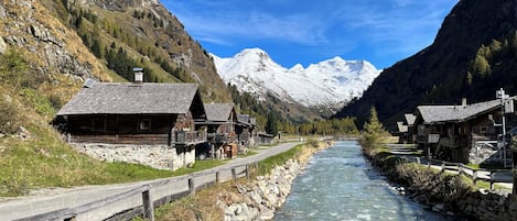 A rustic mountain village with wooden houses along a river, surrounded by snow-capped mountains.