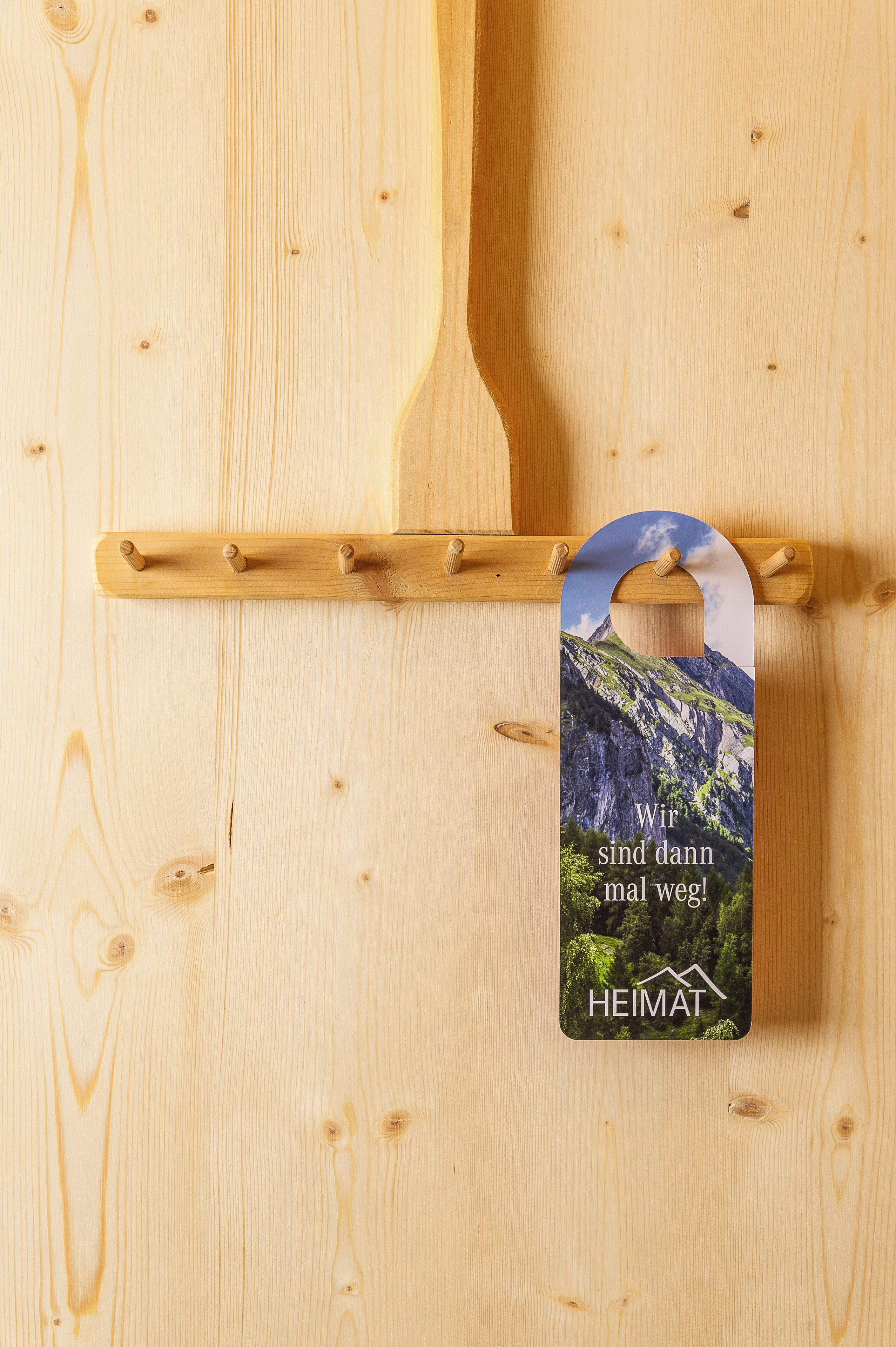 Un mur en bois sur lequel est fixé un panneau perforé en bois, et sur lequel est accrochée une étiquette représentant un paysage de montagne et un texte.