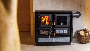 Een houtkachel met een brandend vuur, een bedieningspaneel en een houtmand aan de rechterkant.
