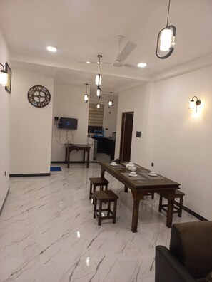 Un comedor con piso de mármol, una mesa de madera y sillas, un reloj de pared, ventiladores de techo e iluminación empotrada.