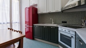 Una cocina con armarios blancos, un refrigerador rojo, un fregadero y un horno.