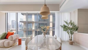 Ein modernes Wohnzimmer mit einem großen Esstisch, bequemen Sitzmöglichkeiten, einem großen Fenster mit Blick auf die Stadt und einer Zimmerpflanze.