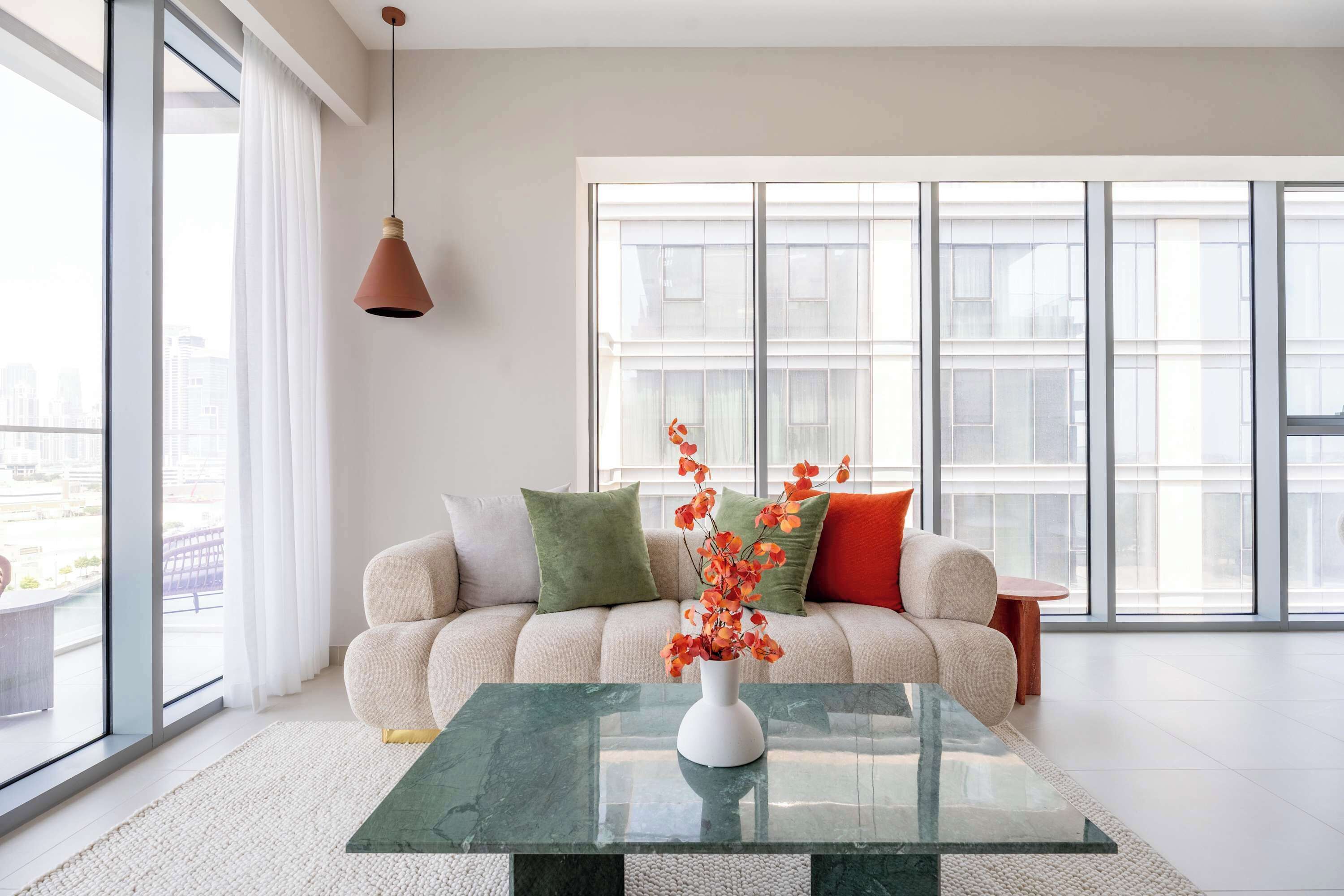 Una sala de estar moderna con un sofá, una mesa de centro de vidrio y un jarrón con flores.