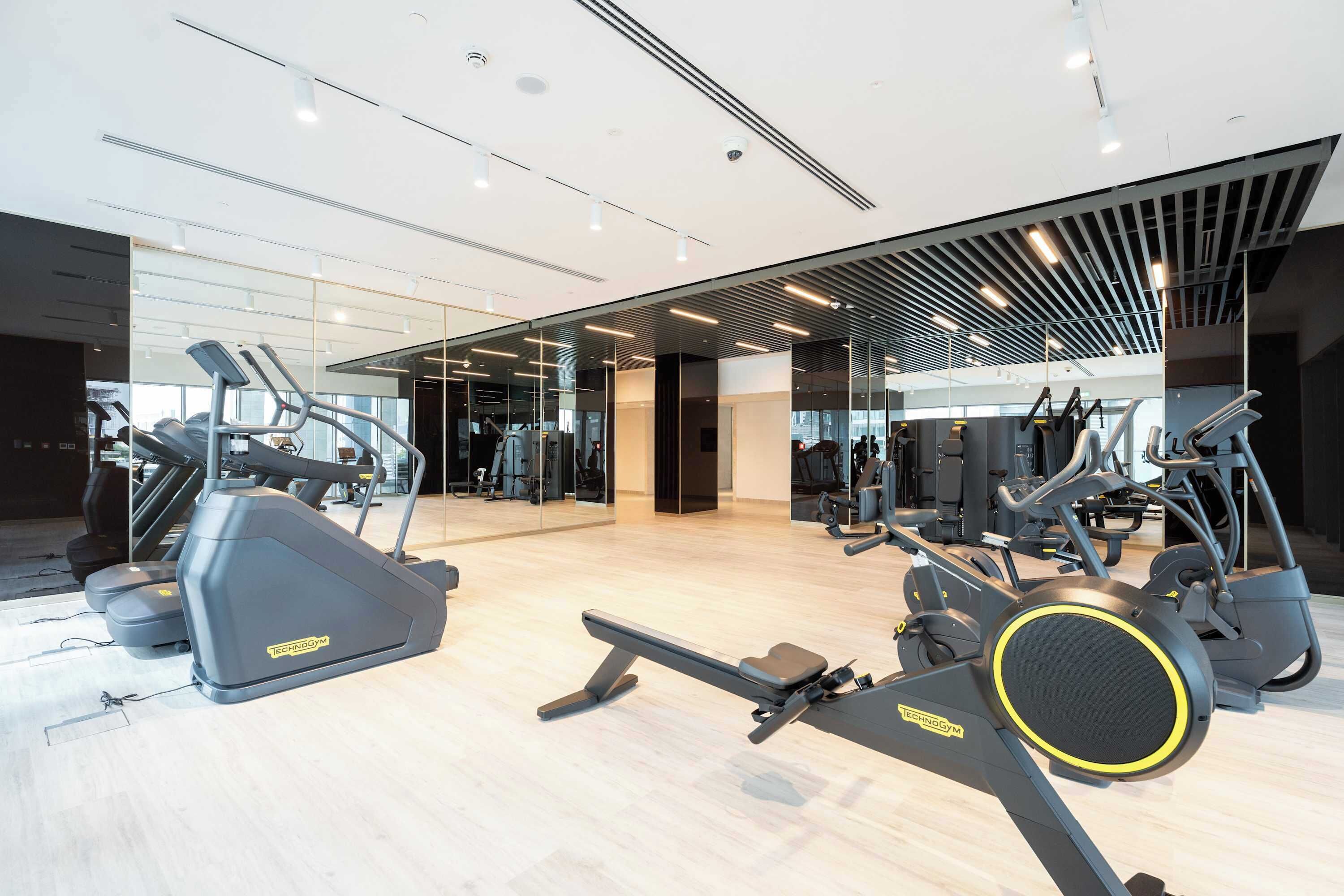 Une salle de sport moderne dotée de nombreux appareils de cardio, notamment des tapis de course et des vélos elliptiques, et offrant un espace généreux avec de grandes fenêtres.