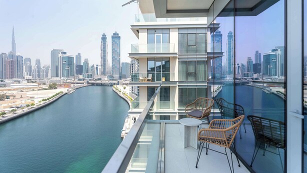 Ein moderner Balkon mit Blick auf die Stadt und einen Fluss, ausgestattet mit Glasgeländern und Korbmöbeln.