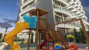 A modern building with a playground in front, featuring slides and swings. - Spacious 1BR with Modern Amenities in Westwood Grande, JVC (Jumeirah Village Circle)