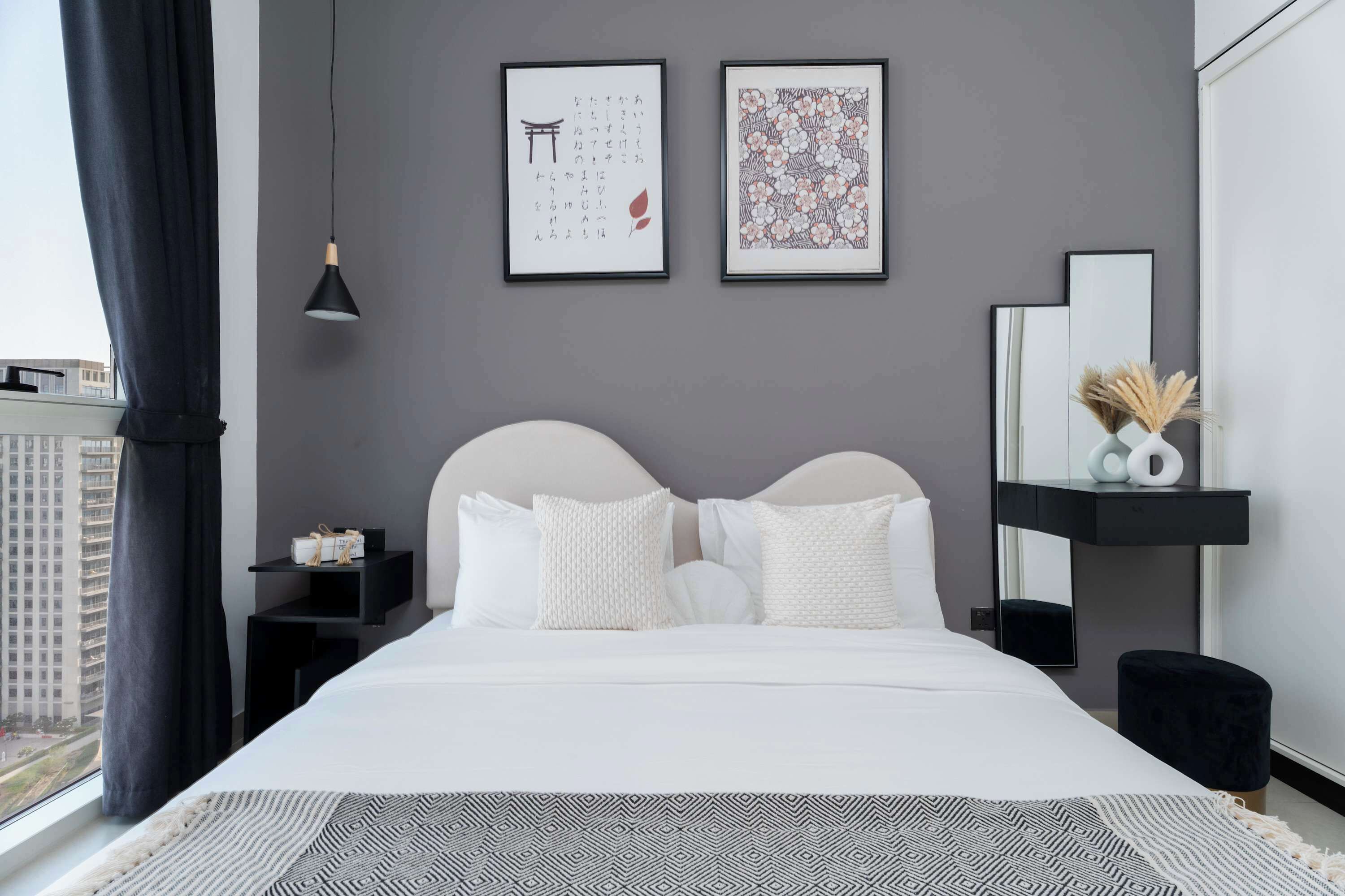 A modern bedroom with a large bed, a nightstand, a bedside table, a mirror, and two framed artworks on the wall.