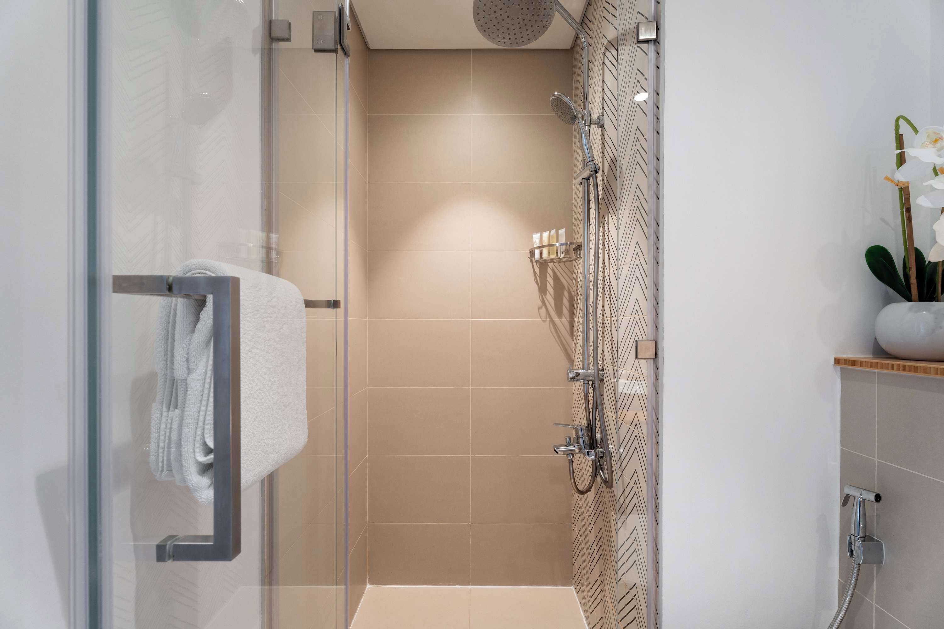 A modern bathroom with a glass shower enclosure, a towel rack, a showerhead, and a decorative orchid plant.