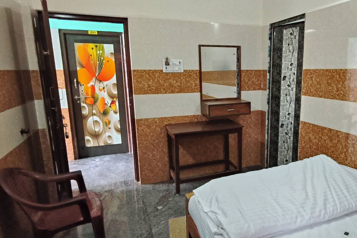 A hotel room with a bed, a desk, a chair, a mirror, and a door with a colorful artwork.