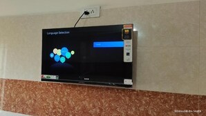 A flat-screen TV mounted on a wall with a language selection screen displaying "HELLO" and "English". - VRS INN (Walajapet)