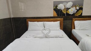 A hotel room with two beds, each with white linens and a wooden headboard. A heart-shaped towel is placed on the bed in the foreground. - VRS INN (Walajapet)