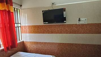 Una habitación con una cama, un ventanal con cortinas rojas, un televisor montado en la pared y un enchufe.