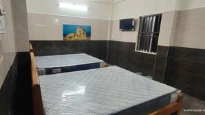 A hotel room with two beds, a painting of a lion, a television, and a window with bars. - VRS INN (Walajapet)