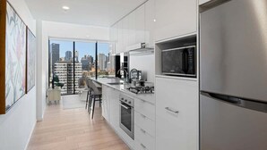 A modern kitchen with white cabinetry, stainless steel appliances, and a city view through large windows. - Top Location Convenient City View Modern Living (Brisbane)