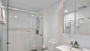 A modern bathroom with a glass shower enclosure, a toilet, and a sink with a mirror. - Top Location Convenient City View Modern Living (Brisbane)