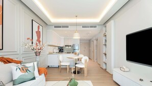 Ein modernes Wohnzimmer mit einer Couch, einem Couchtisch und einem Flachbildfernseher. Es gibt einen Essbereich mit Tisch und Stühlen, und im Hintergrund eine Küche.