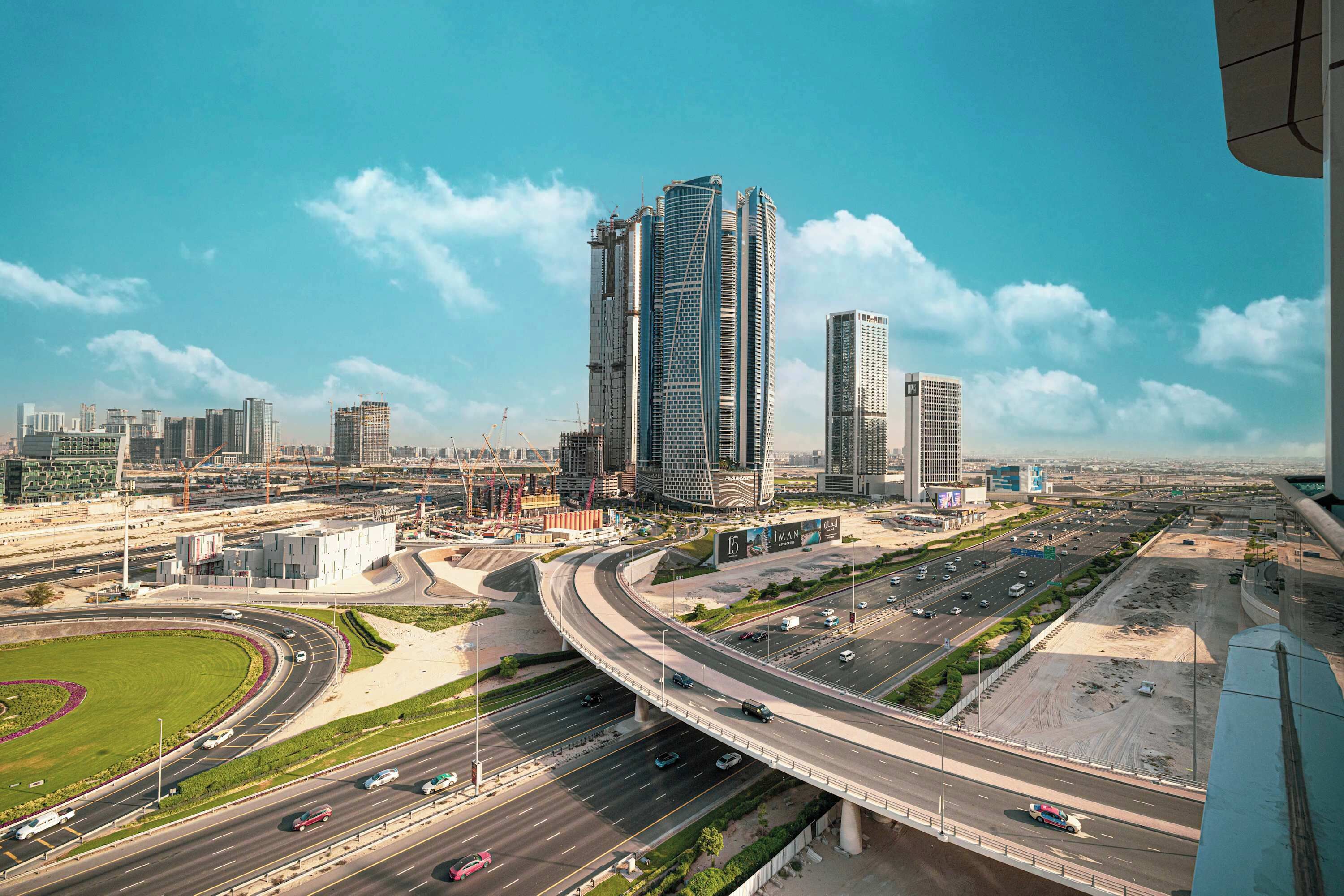 Un paysage urbain avec des immeubles modernes de grande hauteur, une autoroute et un rond-point.