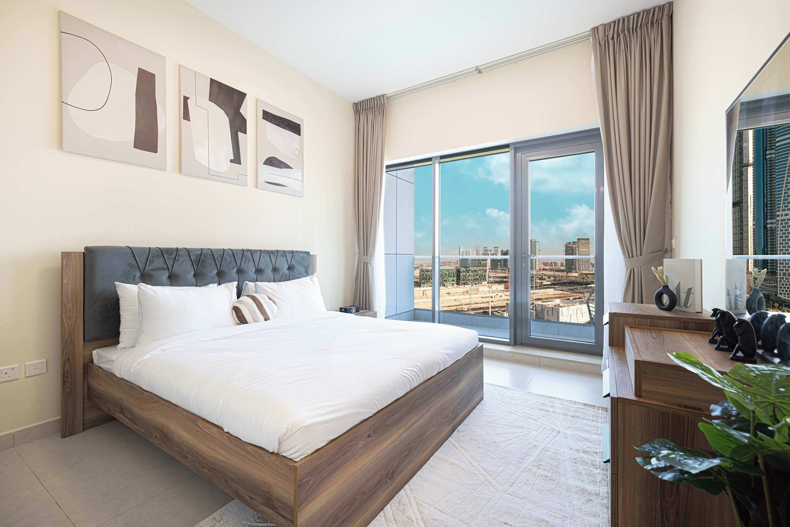 Ein modernes Hotelzimmer mit einem großen Bett, einem Holzkopfende, einem Schreibtisch mit Lampe und Blick auf die Stadt durch große Fenster.
