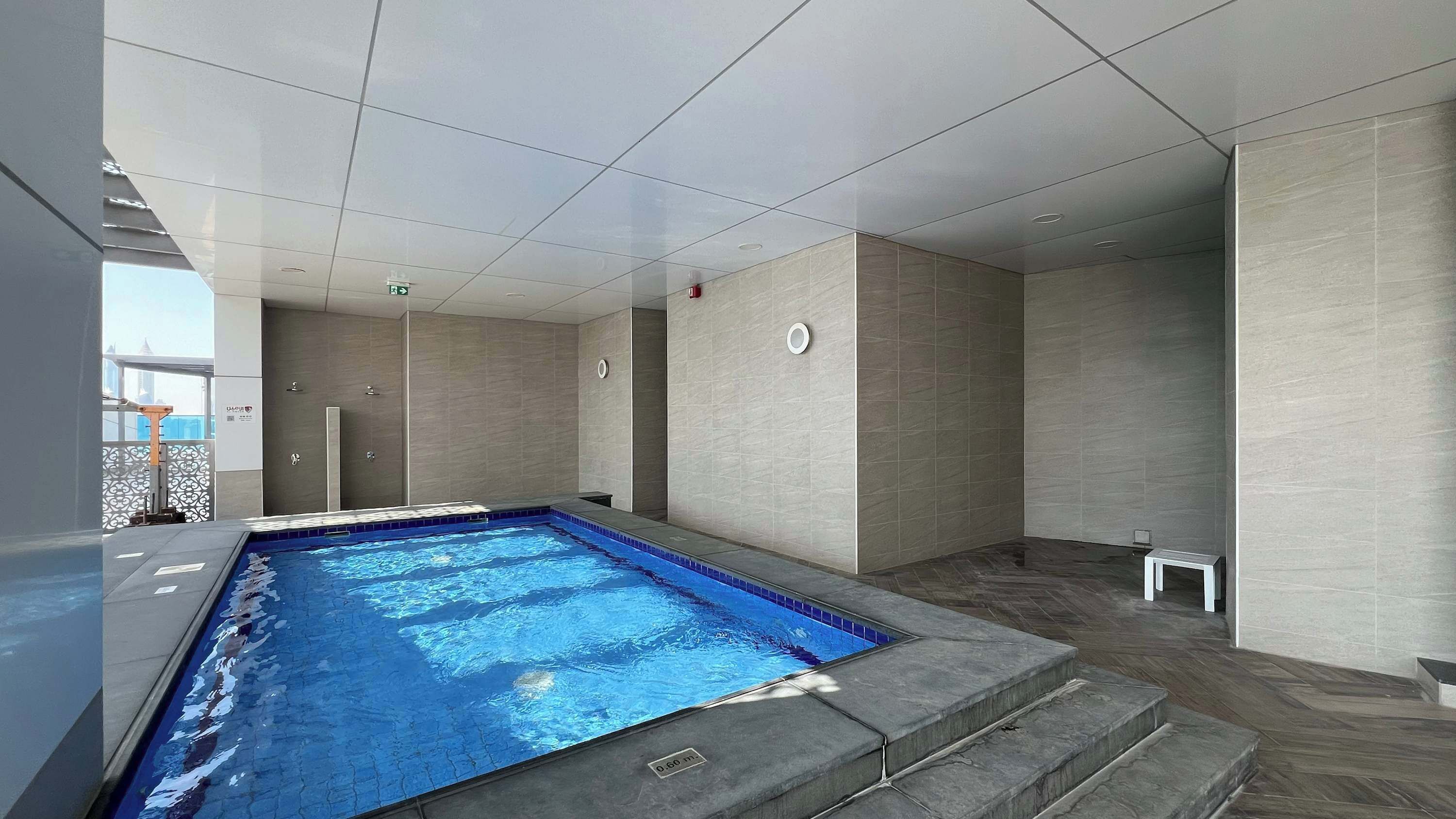 Une piscine intérieure moderne, avec une eau d’un bleu limpide, des murs carrelés et un sol également carrelé.