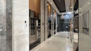 Un pasillo moderno de hotel con suelo de mármol, puertas de cristal y un panel digital del ascensor.