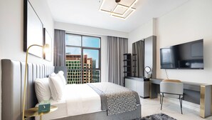 A modern hotel room with a large bed, a desk, a TV, and a view of the cityscape. - Sophisticated 2-Bedroom Hideaway in MEG 318 (Business Bay)