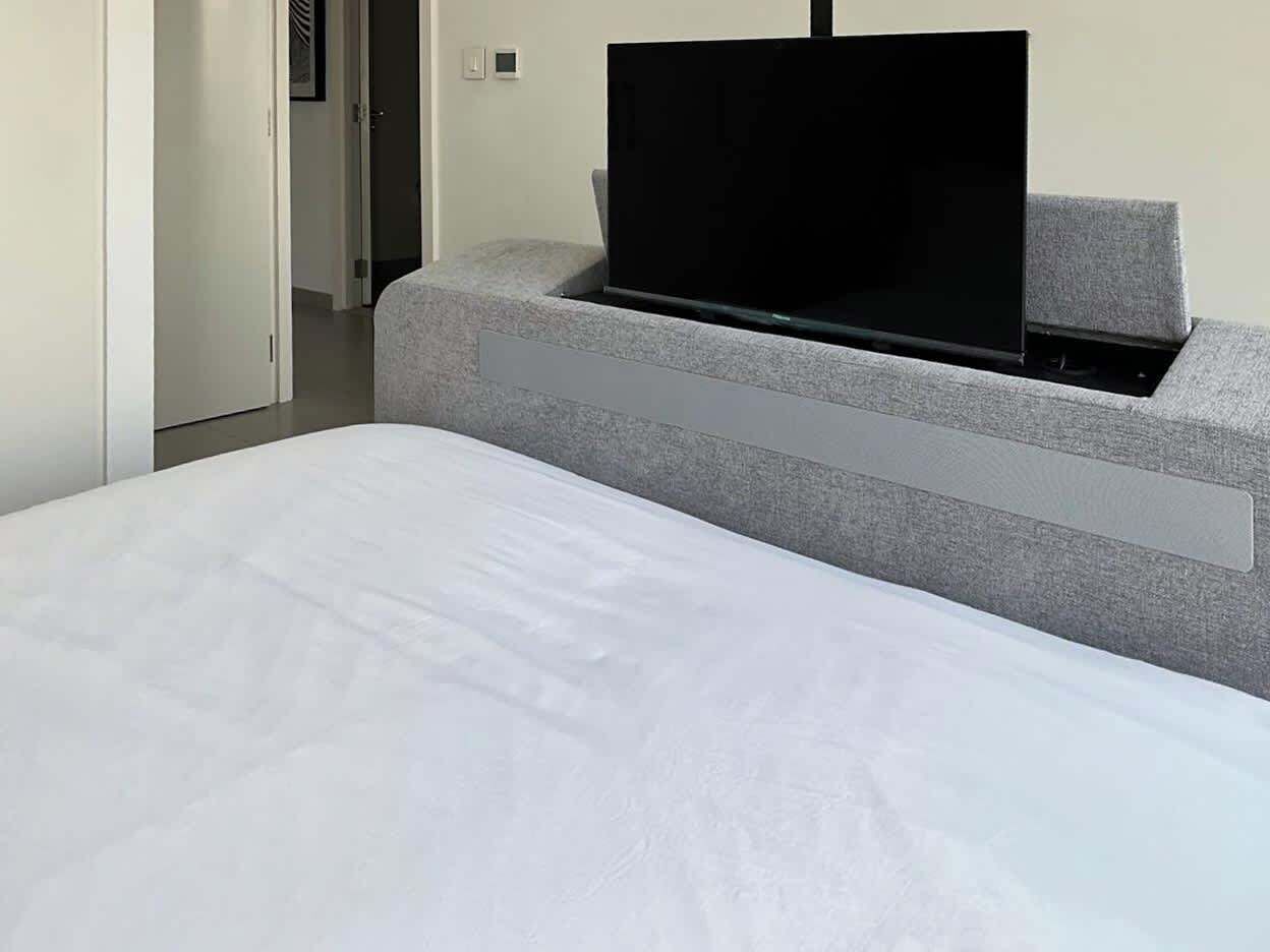 Habitació d'hotel moderna amb un llit, una banca estofada de color gris i un televisor de pantalla plana fixat a la banca.