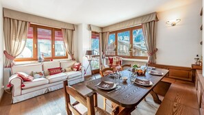 Ein gemütliches Zimmer mit einer Couch, einem Esstisch und großen Fenstern mit Vorhängen.