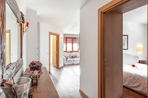 Un pasillo que conduce a un dormitorio con cama, una ventana con cortinas y suelo de madera.