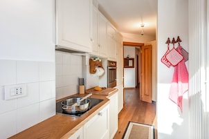 Una cocina con armarios blancos, encimera de madera, estufa y ventana con cortinas.