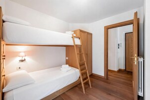 Habitación con literas, una escalera de madera, un armario y una puerta que da a otra habitación.