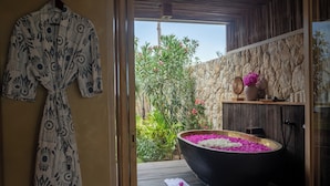 Un área de spa con una bañera negra grande llena de flores rosadas y blancas, un banco de madera y una pared de piedra.
