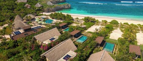 Un resort con edificios de techo de paja, piscina y vista a la playa.