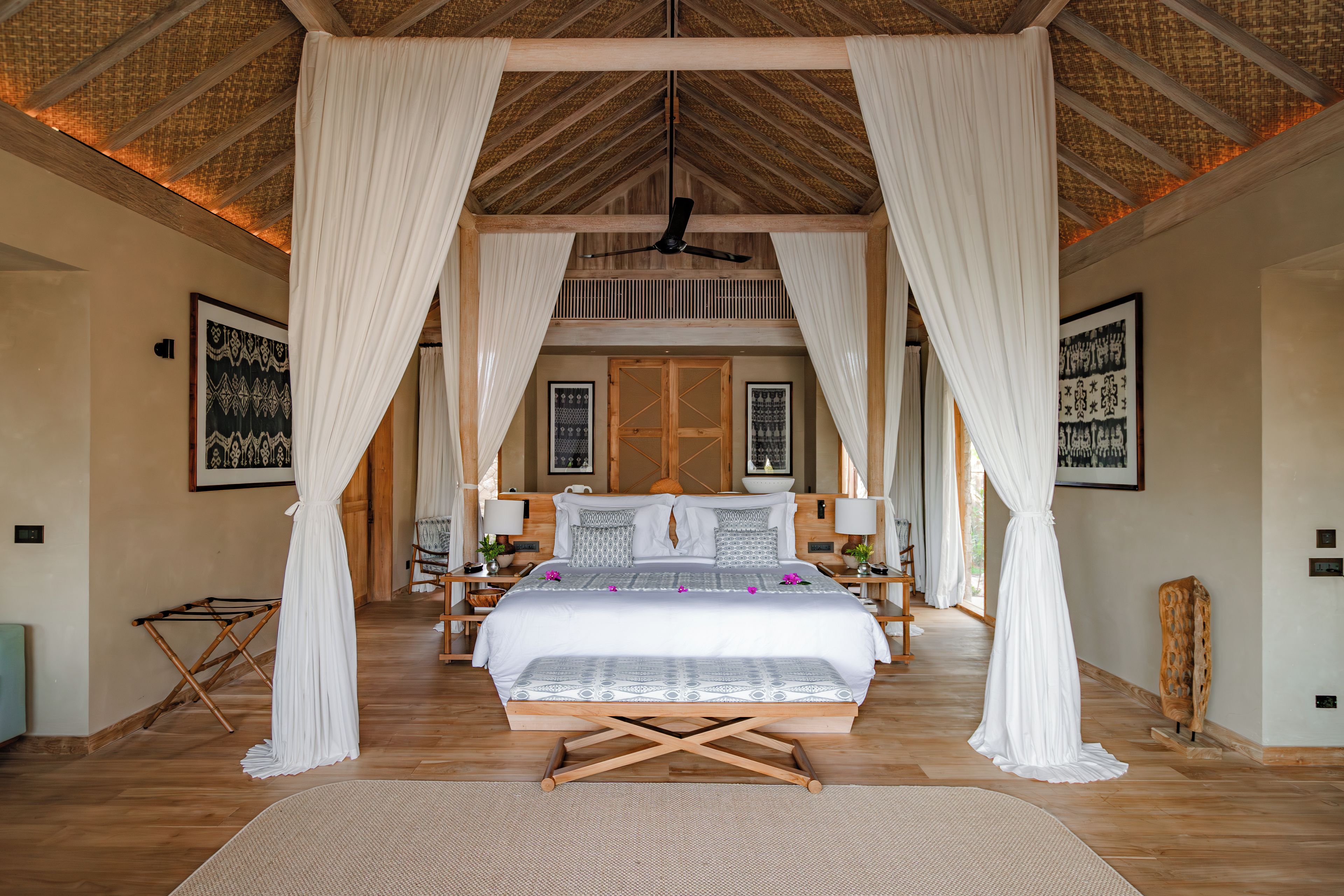 A spacious bedroom with a large bed, a wooden ceiling, and a view of the outdoors.