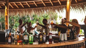 Zona bar con tetto di paglia, travi in legno e diversi bicchieri e bottiglie sul bancone.