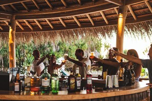 A bar area with a thatched roof, wooden beams, and various bottles and glasses on the counter.