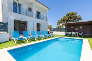 A swimming pool with blue chairs, a wooden deck, and a two-story building with white walls and shutters. - Villa Playa Esperanza by Rentallorca (Playa de Muro)