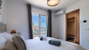 Ett hotellrum med en säng, en lampa, ett fönster med gardiner, en luftkonditioneringsanläggning och en garderob i trä.