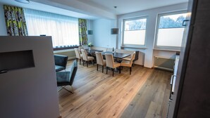 A modern dining area with a wooden table and chairs, large windows with blinds, and a radiator. - Apart Inntalerhof (Toesens)